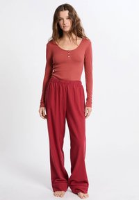 Długa koszula w kolorze rdzy z guzikami oraz luźne spodnie w czerwoną kratkę. Miękka tkanina, casualowy styl i luźny krój.