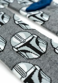 Calze di cotone con un motivo ripetuto di elmi Mandaloriani azzurri su uno sfondo grigio, con un accento blu su una calza.