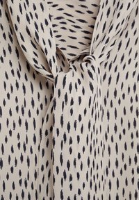 Tissu beige avec un motif de traits noirs irréguliers noué en un nœud lâche, montrant un gros plan sur le matériau et le design.