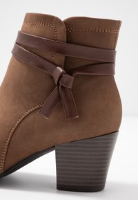 Brązowe zamszowe botki za kostkę z związanym brązowym skórzanym akcentem, z teksturowanym, blokowym obcasem i kontrastowym przeszyciem wzdłuż szwów.