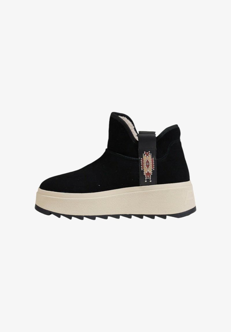 Botines negros de ante con una suela gruesa color crema, que presentan una correa decorativa con adornos y una suela texturizada para mayor tracción.