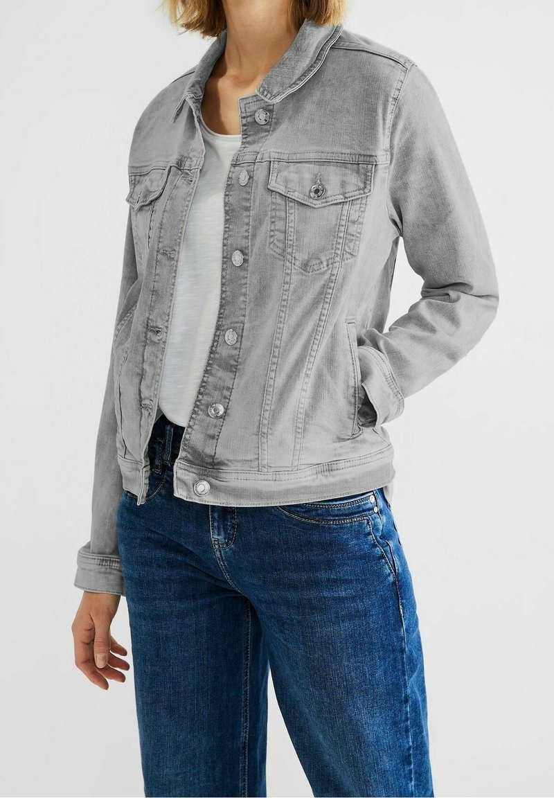 Jasnoszara kurtka dżinsowa z przodu zapinana na guziki, klasycznym kołnierzem oraz dwoma kieszeniami na piersi. Posiada przeszywane szwy i lekko postrzępioną teksturę.