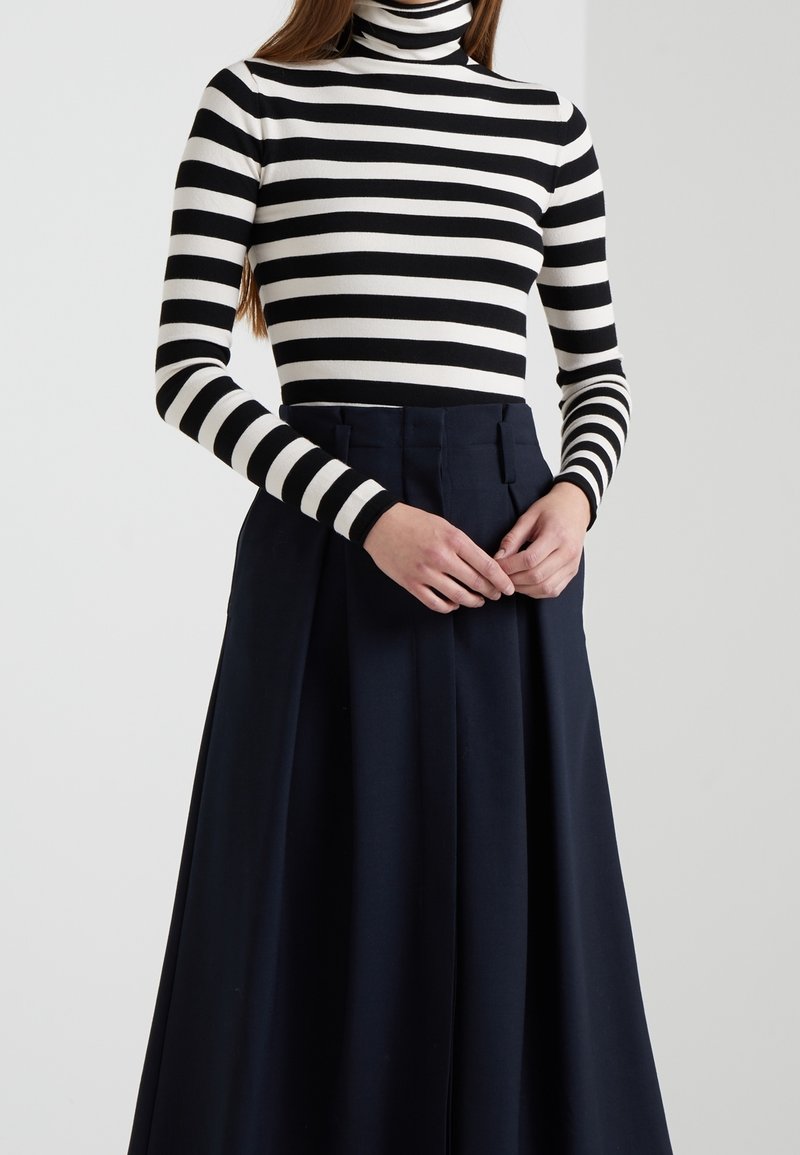 Col roulé rayé en noir et blanc, associé à une jupe bleue marine taille haute avec des plis et une coupe ajustée.