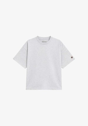 T-shirt gris clair à manches courtes et col rond avec un petit patch logo rond sur la manche gauche et une étiquette "Sweet Pants" à l'intérieur du col.