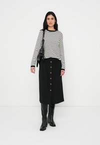 Μπλούζα με μακριά μανίκια σε ριγέ ασπρόμαυρο σχέδιο, συνδυασμένη με μαύρη φούστα έως το γόνατο που διαθέτει κούμπωμα με κουμπιά μπροστά και λεία υφή.