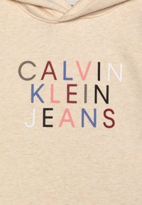 Beige hoodie met een grafische print op de voorkant. De tekst luidt "CALVIN KLEIN JEANS" in verschillende kleuren: zwart, wit, roze, rood, blauw en grijs.