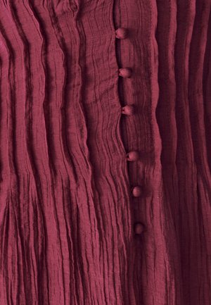 Bordeauxkleurige textuurstof met verticale plooien en zes ronde stoffen knopen in het midden. Subtiele glans en zachte uitstraling.
