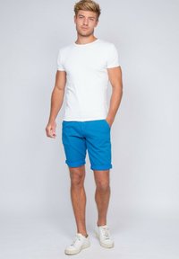 T-shirt blanc à manches courtes associé à un short en denim bleu retroussé et des baskets blanches, avec un design ajusté et une texture en coton lisse.