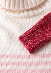 Maglione lavorato a maglia con un corpo a righe crema e rosa e un colletto alto rosso mélange. Polsini a coste e texture morbida.
