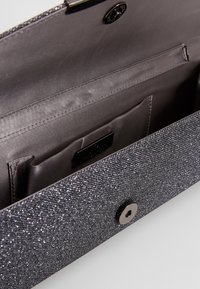 Cartera de mano gris con un acabado de purpurina texturizada, que presenta un cierre a presión, ranuras para tarjetas en el interior y un forro suave.