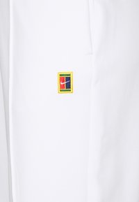 Baltie sporta šorti, izgatavoti no gludas auduma, ar nelielu, daudzkrāsainu Nike logotipu izšūtu apakšējā priekšpusē.
