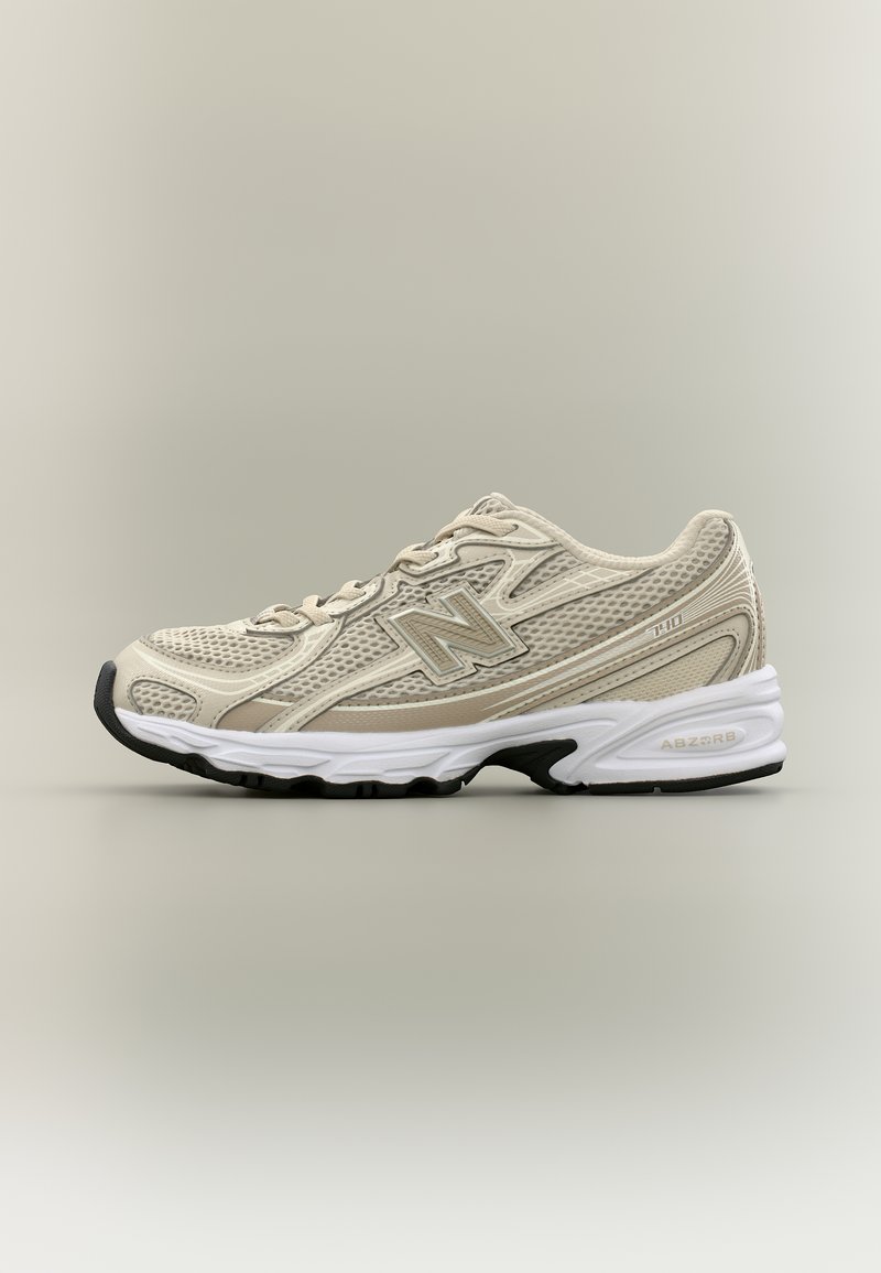 Μπεζ αθλητικό παπούτσι New Balance με επάνω μέρος από δίχτυ, λευκή ενδιάμεση σόλα, μαύρη εξωτερική σόλα και λογότυπο "N" στη πλευρά, εμφανιζόμενο από την εσωτερική πλευρά.