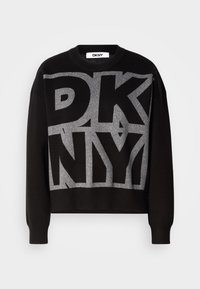 Melnā džemperis ar īsu dizainu, kas rotāts ar lielām sudraba spīdīgas tekstas burtiem "DKNY" priekšpusē. Mīksta adījuma tekstūra; apaļa dekoltē.