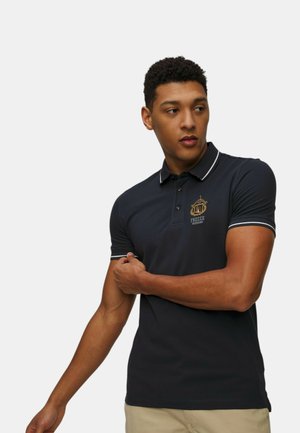 Polo shirt blu navy con un logo sul petto, dotato di accenti bianchi sul colletto e sui bordi delle maniche, realizzato in un tessuto liscio.