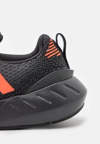 Svart idrottssko med en texturerad stickad ovandel, djärva röda accenter, en vadderad svart sula och en subtil logotyp på hälen.