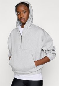 Ανοιχτό γκρι φούτερ με φερμουάρ, με μπροστινή τσέπη, μεγάλο κουκούλι, ριμπ τελείωμα και λογότυπο Under Armour. Το ύφασμα φαίνεται μαλακό και άνετο.