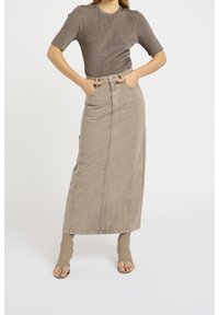 Falda maxi de mezclilla beige con bolsillos frontales, detalles en costuras verticales y cintura alta. Combinada con un top marrón texturizado y ajustado, y calzado beige.