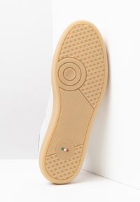 Hvid sneakersål med en tekstureret gummibund. Har et cirkulært design-element og et prægede logo på siden.
