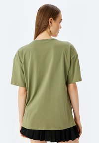 Una camiseta verde oliva de manga corta, con cuello redondo y corte holgado, combinada con una falda negra plisada que muestra una textura suave.