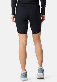 Shorts da bici neri a coste realizzati in materiale elasticizzato, caratterizzati da una lunghezza a metà coscia, abbinati a sneaker grigie chiare con suole bianche.