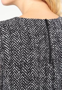 Černé šaty s bílým herringbone vzorem, s zadním zipem a hladkým, textured materiálem.