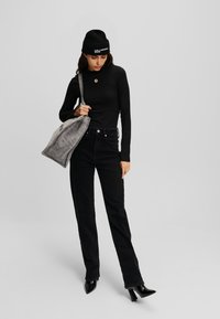 Top negro de manga larga con cuello redondo, combinado con unos vaqueros negros de talle alto. Lleva un bolso tote texturizado gris y un gorro de punto negro.