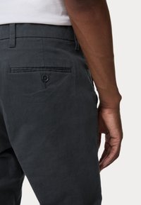 Donkergrijze broek van een gladde stof, met een achterzak met knop en een slank, op maat gemaakt ontwerp.