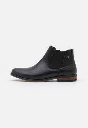 Botte Chelsea en cuir noir avec panneaux latéraux élastiques, talon empilé marron et bout arrondi, montrée de profil sur fond blanc.