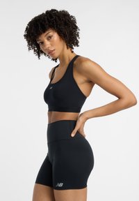 Top de sport noir court et shorts taille haute avec une texture lisse. Comprend un logo sur les shorts, un décolleté plongeant et un design dos nageur.