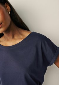 Marinblått t-shirt med rundad hals och uppvikta korta ärmar, tillverkat av mjuk bomull. Slät textur och avslappnad passform. Minimal sömnadsdetaljer.