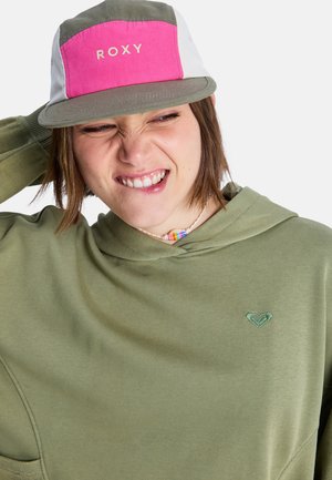 Pull-over à capuche vert avec une poche avant. Casquette rose clair et grise avec le logo "ROXY". Collier de perles remarquable avec un motif coloré.