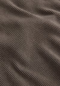 Barna bordázott anyag, amelynek texturált felülete van, keskeny függőleges csíkokkal, puha és rugalmas anyag.