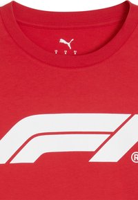 Raudona medvilninė marškinė su dideliu baltu „Formula 1“ logotipu. Apykaklės kraštas su raukiniais, viduje yra ženklinimas.