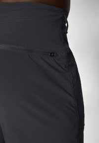 Sorte idrettsshorts med en glatt tekstur, som har en sidelomme med glidelås og forsterkede sømmer for holdbarhet.