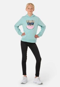 Felpa azzurra chiara con un'illustrazione di un carlino che indossa occhiali da sole e una fetta di anguria, abbinata a jeans skinny neri e sneakers bianche.