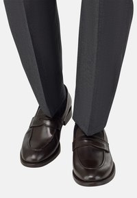 Hnědé kožené mokasíny s kulatou špičkou a páskem, kombinované se šedými vzorovanými kalhotami s jemnou texturou.