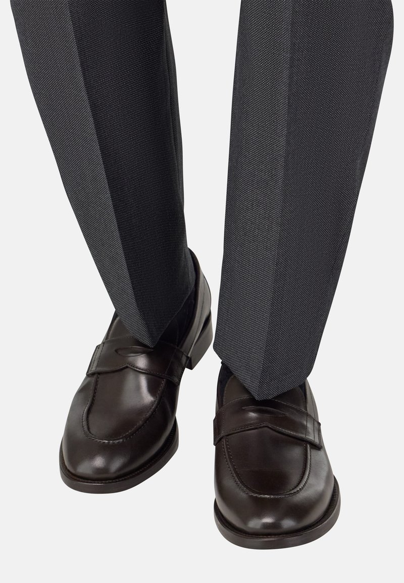 Hnědé kožené mokasíny s kulatou špičkou a páskem, kombinované se šedými vzorovanými kalhotami s jemnou texturou.