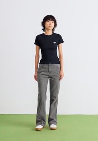 Sort bomulds t-shirt med et lille logo, parret med grå flared jeans og hvide sneakers. Simpelt design med en tætsiddende silhuet.