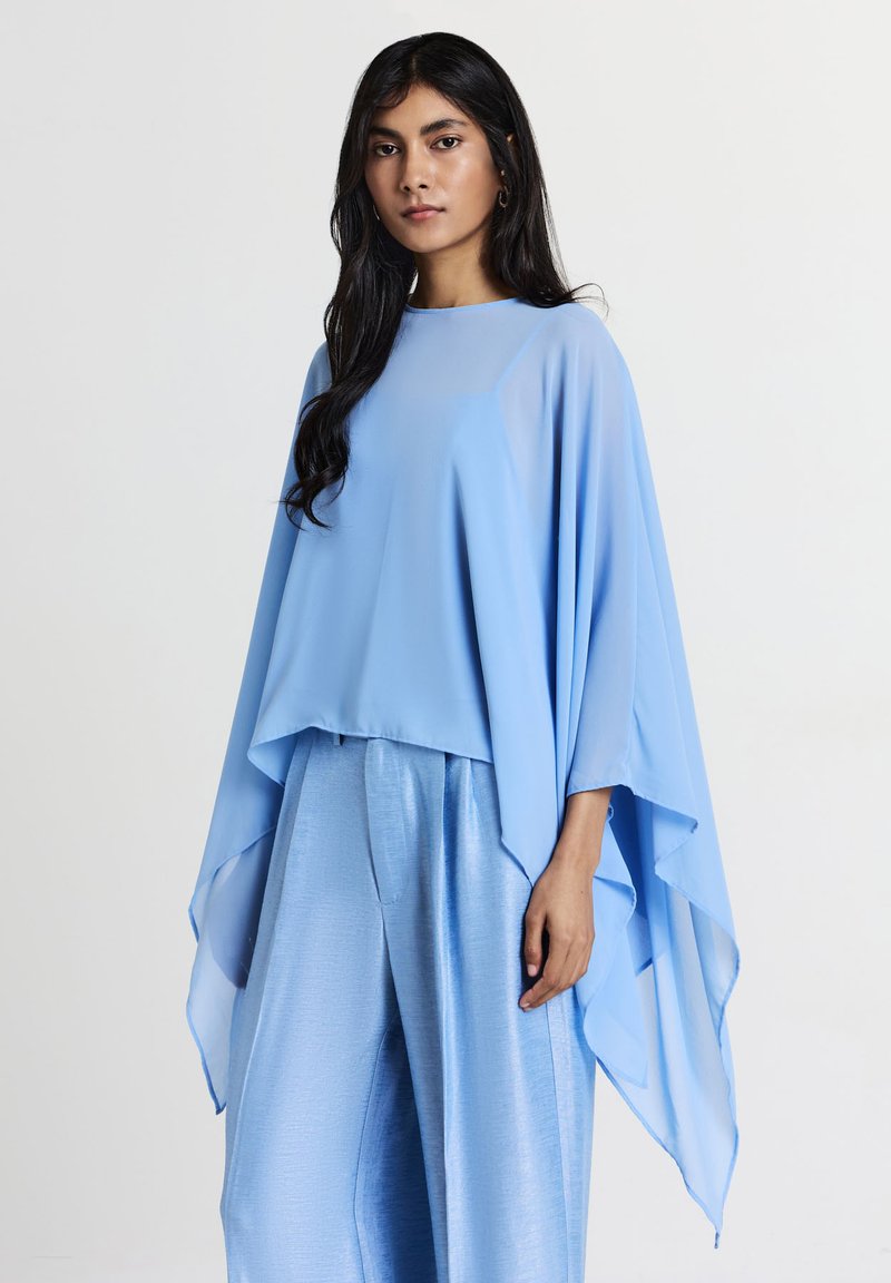 Top azzurro chiaro, trasparente, con maniche fluide, abbinato a pantaloni azzurro chiaro lucidi e plissettati. Tessuto morbido con una silhouette drappeggiata.