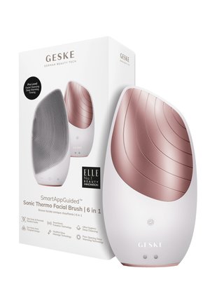 Brosse de visage thermo-sonique avec un corps blanc, des accents en or rose, une surface en silicone texturée et un design épuré. Boîte incluse.
