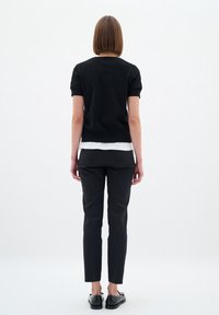 Black short-sleeve knit top layered over a white long-sleeve shirt, paired with black slim-fit pants and black slip-on shoes.