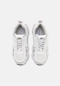 Chaussures de sport blanches avec tige en mesh et synthétique, accents gris, design à lacets et col rembourré. Présentent le logo de la marque sur la languette.