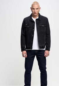 Černá džínová bunda, zapínání na knoflíky, dvě náprsní kapsy, moderní střih. Nesušená přes bílé tričko a tmavě modré slim fit džíny.