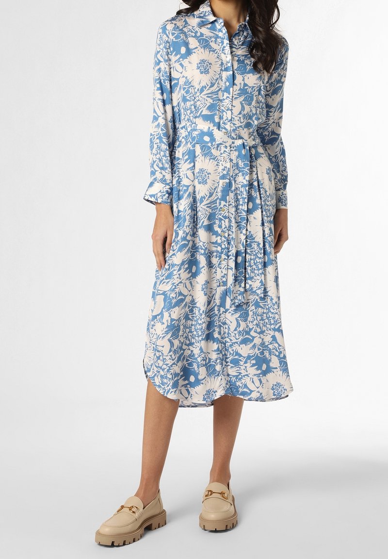 Vestito floreale blu e bianco con maniche lunghe, chiusura anteriore con bottoni, vita con cintura e lunghezza midi; abbinato a mocassini in pelle beige.