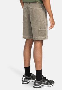 Shorts cargo in un verde oliva sbiadito, realizzati in un tessuto resistente e con numerose tasche. Abbinati a scarpe da ginnastica nere e calzini al polpaccio.