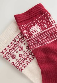 Gestickte Socken in Rot und Creme mit winterlichen Mustern. Die rote Socke zeigt Häuser; die cremige Socke hat geometrische Motive. Strukturierten Bündchen.