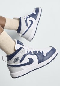 Hvite og marineblå høye sneakers med skinnøvre, perforert tå og polstret krave. Har logo på hælen og kontrastfargede snører.