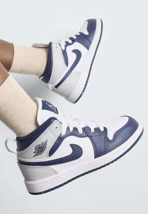 Baskets montantes blanches et marines avec tige en cuir, bout perforé et col rembourré. Présente un logo sur le talon et des lacets contrastés.