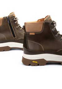 Botas de senderismo de cuero marrón con acentos en tono beige, superficie texturizada, ojales de metal y una suela de goma Vibram en blanco y marrón que contrasta.