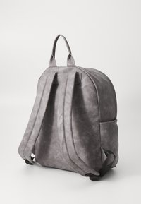Gray backpack with a soft, textured surface, dual shoulder straps, top handle, and side pocket, featuring a rounded design.